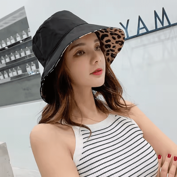 Une femme porte un bob chapeau réversible noir avec une doublure style léopard sur un décor grisé